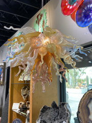 Hand-blown glass chandelier in amber, toffee, pink and clear curling tendrils hanging by a gallery window