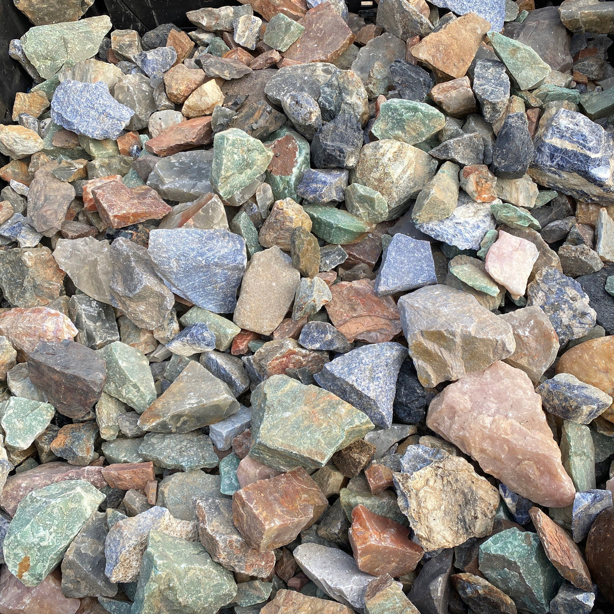Rough Brazilian minerals heaped in a crate, green aventurine, blue sodalite, rose quartz and jasper