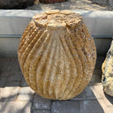 Upright red travertine barrel cactus carving fountain with fine ribbing against a concrete curb