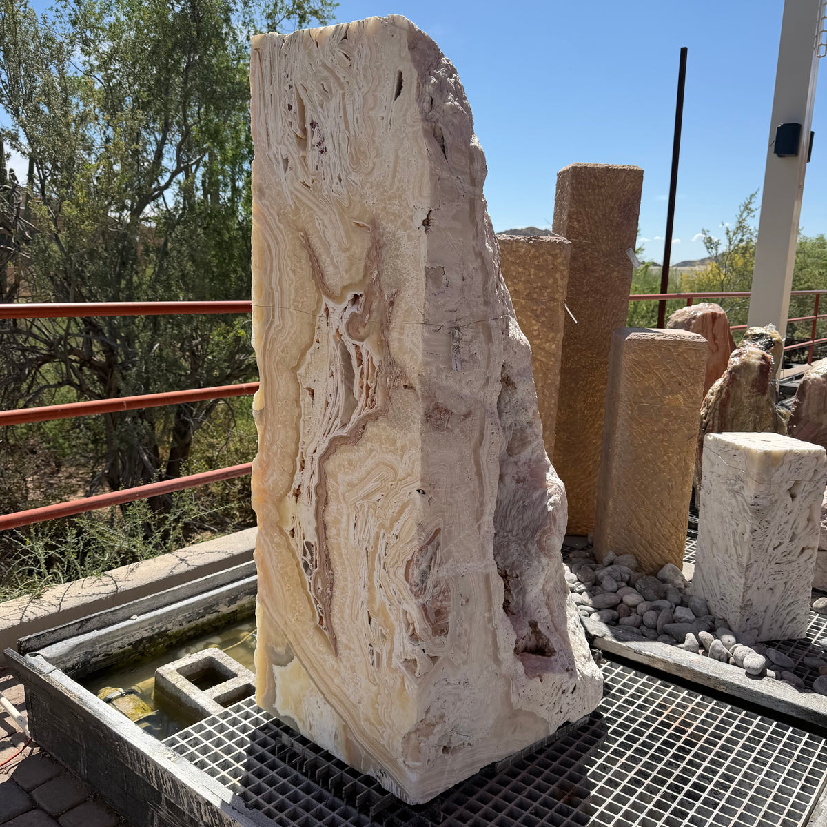 Sunset Fossil Onyx boulder fountain with cavern, full banded front face above a water basin grate outdoors