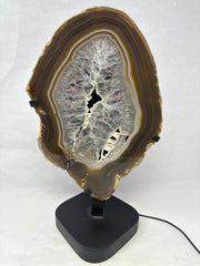 Unlit chocolate agate slice with amethyst center, brown banding and gray crystal core on black stand, front