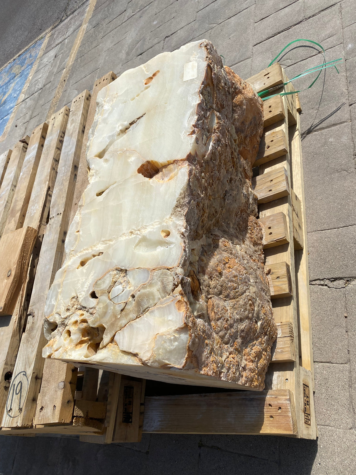 Tekkis Ice Onyx fountain stone on a pallet, glassy white cut face beside a rough amber natural rind
