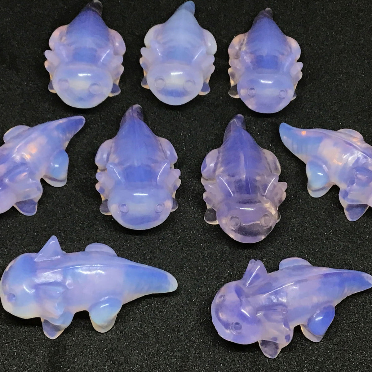 Group of pink opalite axolotl carvings in lavender translucent stone on a black background