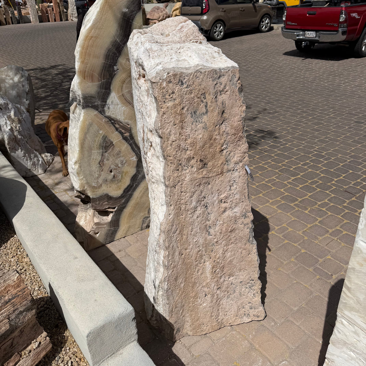 White travertine onyx fountain vertical block, rough natural back face in sunlight on paver courtyard