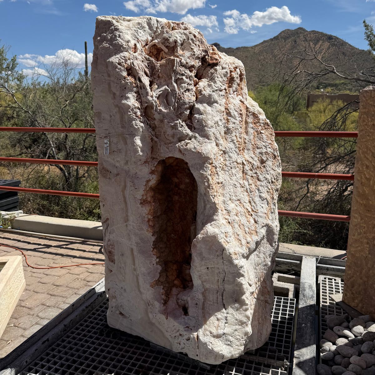 Sunset Fossil Onyx boulder fountain with cavern, crystal-lined hollow opening under blue desert sky