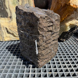 Black marble chiseled block fountain running without a basin on a display grate beside onyx slabs