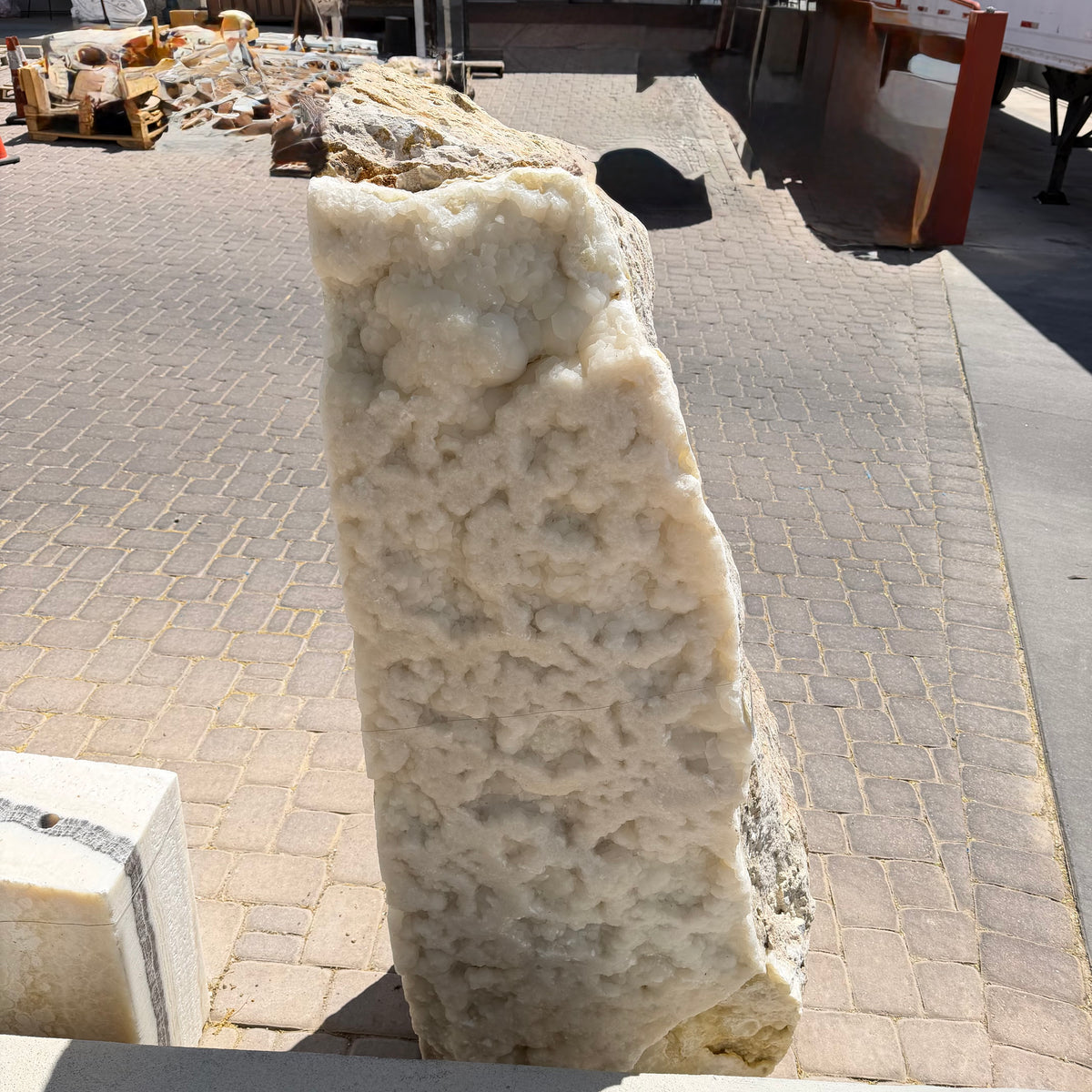 Ice onyx and caliche vertical fountain seen close up, bumpy white druze crystal face above a paver courtyard