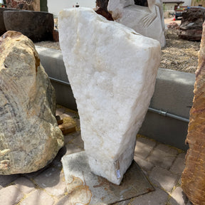 Ice White Onyx Fountain standing upright on a steel base plate, crystalline white face lit in an outdoor stone yard