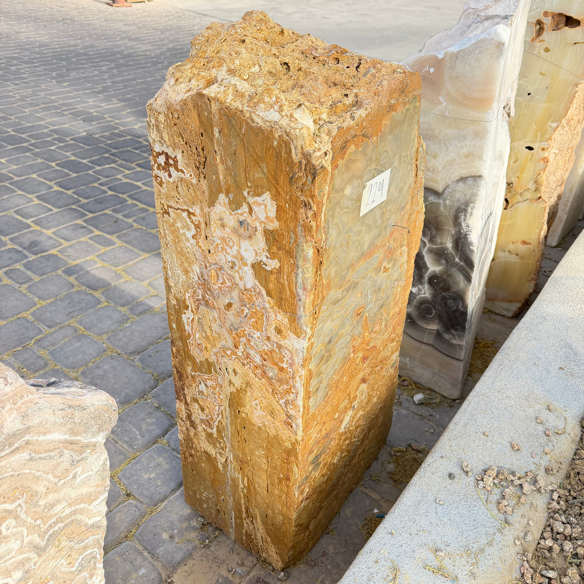 Angled view of the gold travertine onyx fountain monolith showing two cut faces on a stone paver patio