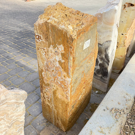 Angled view of the gold travertine onyx fountain monolith showing two cut faces on a stone paver patio