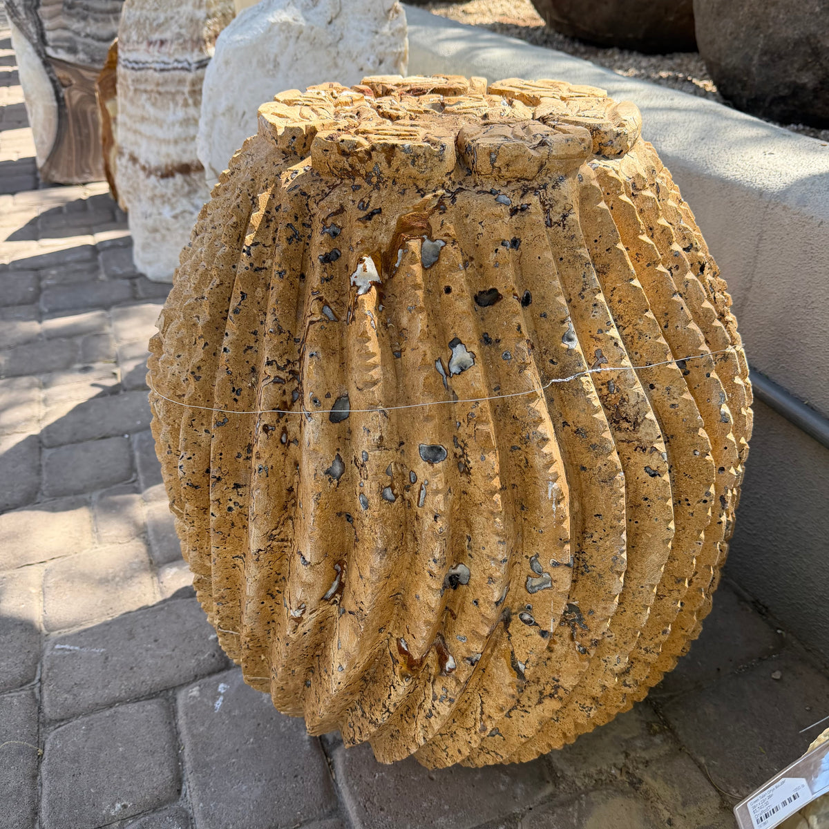 Sunlit red travertine barrel cactus carving showing dark mineral inclusions across its ribs