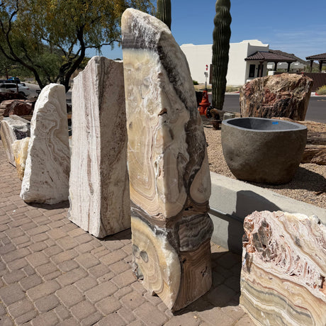 Cosmic Orange Zebra Onyx fountain seen from the side beside other onyx slabs under desert saguaros
