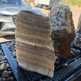 Serpentine onyx layered boulder fountain with one flat cut side, water bubbling over honey-banded rock