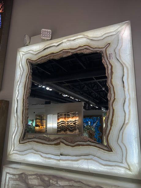 Backlit gray onyx square mirror with cream and brown banded stone frame glowing on a gallery wall