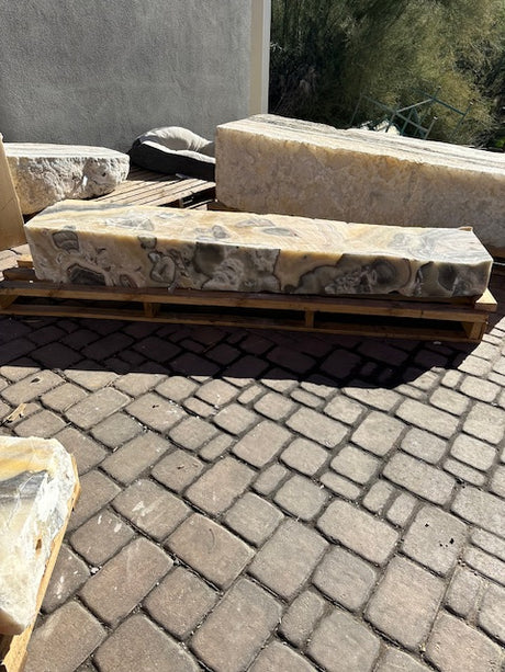 Cosmic onyx fountain pillar resting on a wooden pallet, polished wavy face with gray vugs seen from the side