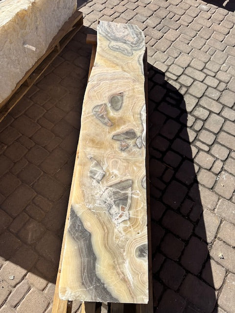 Cosmic onyx fountain pillar on a pallet, wavy cut side with honey and gray banding, viewed from above