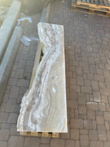 Vertical hourglass amber onyx fountain slab showing cream and tan banding, laid lengthwise on a pallet outdoors