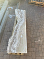 Vertical hourglass amber onyx fountain slab showing cream and tan banding, laid lengthwise on a pallet outdoors