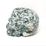 Green and white moss agate skull carving, back-left view with dendritic veining and open druzy pockets