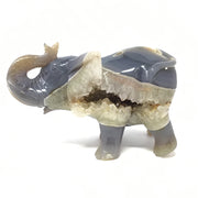 Gray agate elephant carving with trunk up, druzy quartz geode pocket exposed on its side