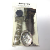 Smudge Kit contents through the clear pack: charcoal disc, sweetgrass braid, sage stick, shell and feather