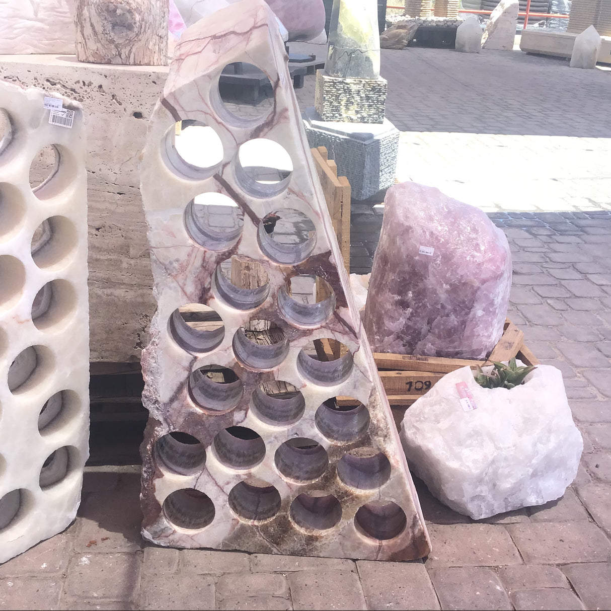 Serpentine onyx wine rack with 21 drilled holes in pink-veined cream stone, shown outdoors
