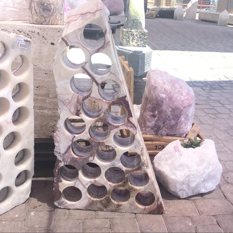 Serpentine onyx wine rack with 21 drilled holes in pink-veined cream stone, shown outdoors