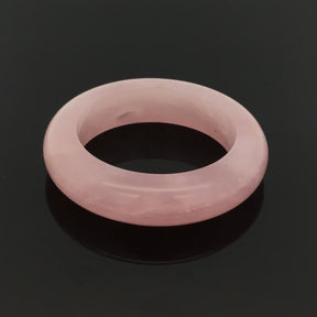 Glossy rose quartz stone band ring carved from a single piece, three-quarter view on black