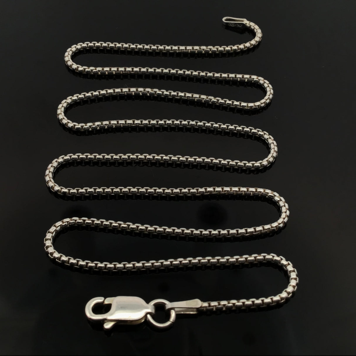 18-inch round box chain 028 coiled in an S curve on glossy black with the lobster clasp at front