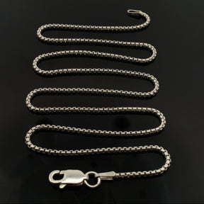 18-inch round box chain 028 coiled in an S curve on glossy black with the lobster clasp at front