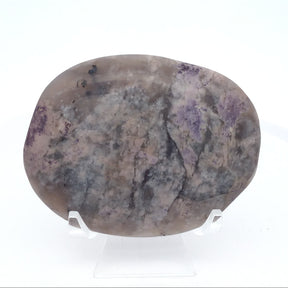 Oval palm stone, pale mauve and gray with scattered purple flecks, upright on a clear stand