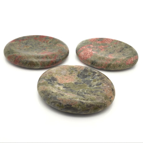 Three oval Unakite wishing stones with a thumb divot, mottled green and salmon pink, angled view