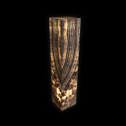Black Zebra Onyx floor pedestal luminary lit from within, warm glow through dark chevron banding