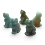 Four carved amazonite sitting cat figurines in mint green and caramel tones on a white surface