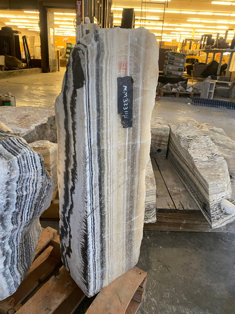 Tapered Yellow Zebra Onyx pillar fountain with bold black and cream striping in a stone warehouse