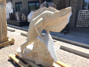 Beige travertine iguana carving climbing a pale rock, front three-quarter view outside a stone showroom
