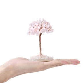 Pale pink rose quartz gemstone chip tree held in a hand on an agate slice base