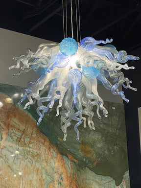 Clear glass chandelier with ink blue and aqua accents, featuring swirling tentacle-like shapes and a textured backdrop.