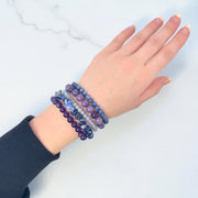 Five meditation intention beaded bracelets in purple and blue stones stacked on a wrist