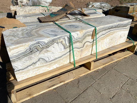 Zebra fossil onyx pillar fountains stacked on pallets, side faces showing rippled grey and cream pin patterns