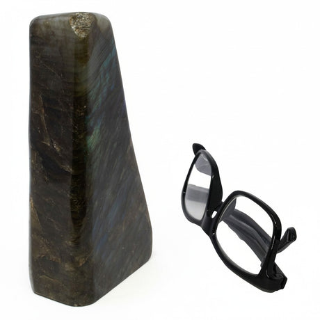 Rare Earth Gallery polished labradorite freeform stone with iridescent blue and gold flashes next to black glasses