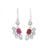 A pair of silver drop earrings featuring oval pinkish-red cabochon gemstones surrounded by clear round and teardrop-cut stones, shown against a plain white background.