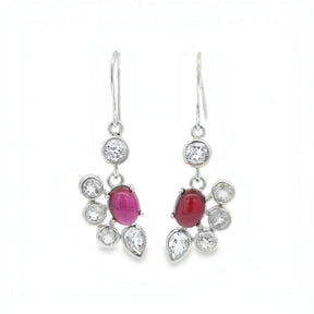 A pair of silver drop earrings featuring oval pinkish-red cabochon gemstones surrounded by clear round and teardrop-cut stones, shown against a plain white background.